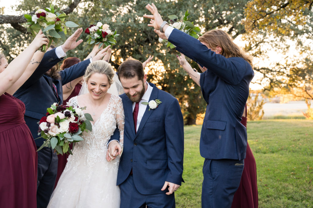 Bride and groom make their way down through their bridal party who are making an arch. Their wedding color palette includes burgundy, silvery white and light pink. 