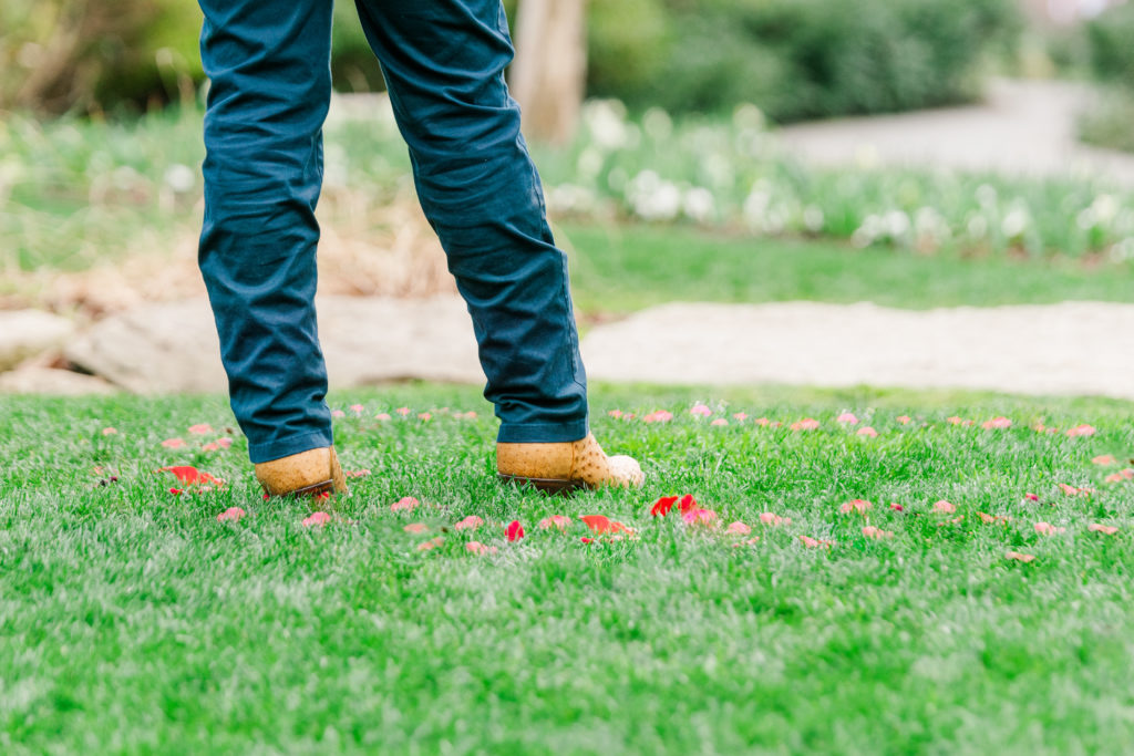 A man's cowboy boots stand on a hill surrounded by a circle of rose petals during his Dallas Arboretum Proposal. 