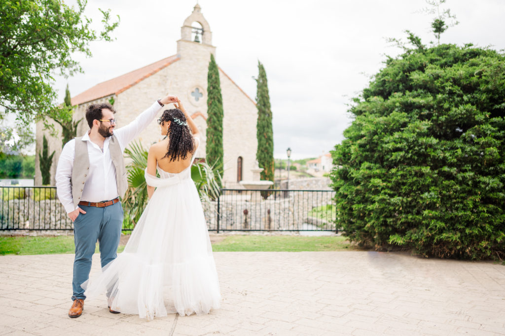 Bride and groom do a spin in front of Bella Donna Chapel as part of the Adriatica Village elopement.