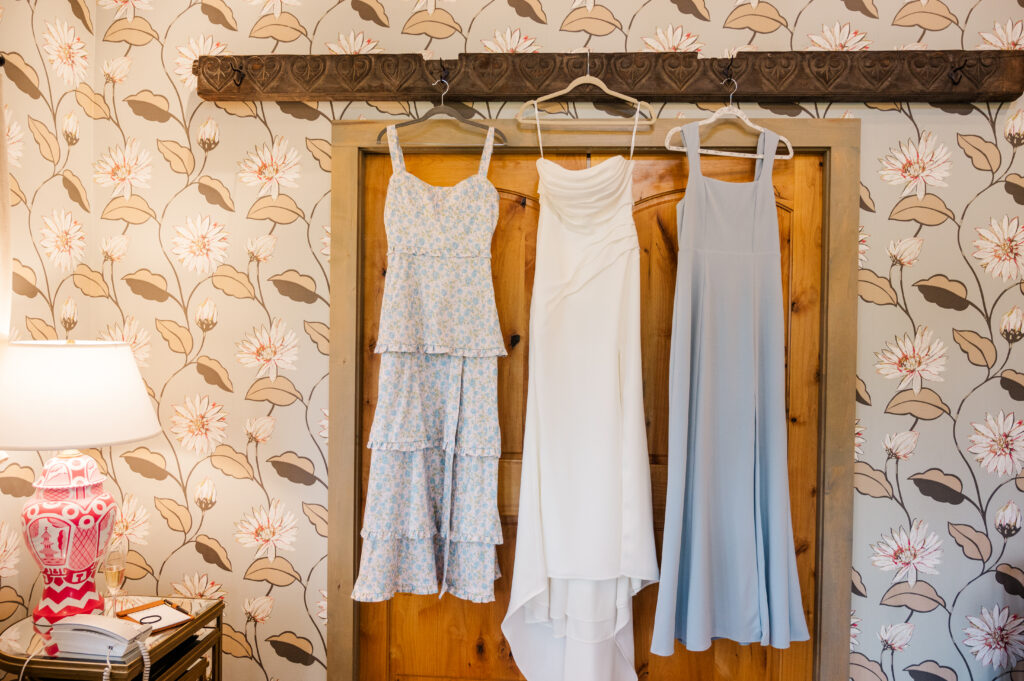 Bridal gown and two bridesmaids dresses hang in a cabin at Camp Lucy